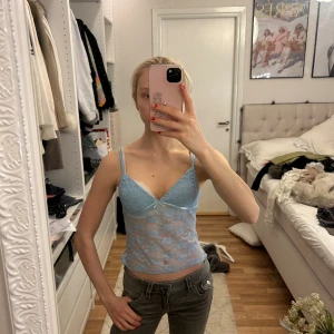 Blå spetslinnetopp från Chiquelle - Säljer en ljusblå spetslinnetopp från Edikted med smala axelband och en liten rosett framtill. Toppen är genomskinlig och har ett feminint, tight passform som framhäver siluetten. Perfekt för att skapa en trendig look