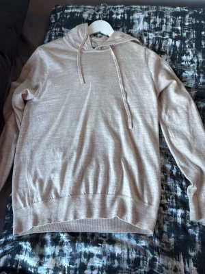 Beige hoodie från alqvist 100% merino - Säljer en stilren beige hoodie med huva och dragsko. Tröjan har ribbade muddar vid ärmslut och nederkant, och är tillverkad i ett mjukt material som känns skönt mot huden. Perfekt för dig som gillar en enkel och clean look.(100% merinoull) 