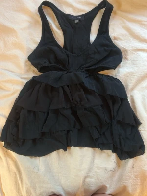 Svart volang linnetopp från bershka  - Säljer en svart linnetopp från bershka, aldrig använd men utan prislappen kvar. Den sitter tajt där uppe och sedan går det ut men volanger. 