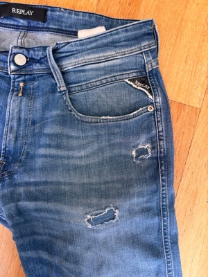 Blå slitna Replay jeans - Säljer ett par blå jeans från Replay med slitningar och distressed detaljer på benen. Jeansen har klassisk femficksdesign, smal passform och är gjorda i denim. Jeansen är i storlek w31 l34