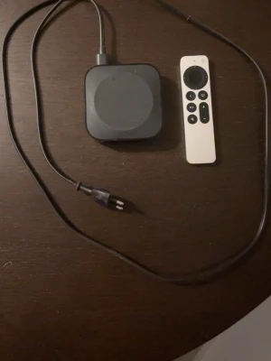 Apple TV med fjärrkontroll och sladd - Säljer en Apple TV med tillhörande fjärrkontroll och strömkabel. Boxen är svart och fjärrkontrollen är silverfärgad med svart touchyta och knappar. Perfekt för streaming och appar direkt till din TV.