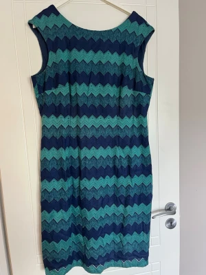 Blågrön mönstrad ärmlös klänning - Snygg ärmlös klänning med zigzag-mönster i blått och grönt. Klänningen har en v-ringad rygg och rak passform som slutar strax ovanför knäna. Perfekt för dig som gillar färg och mönster. Materialet känns som bomull eller polyester.