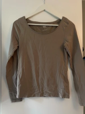 Beige långärmad topp från 157 - En enkel och stilren beige långärmad topp från 157 med rund halsringning. Tillverkad i mjuk bomull som känns skön mot huden. Perfekt att matcha med jeans eller kjol för en clean look.