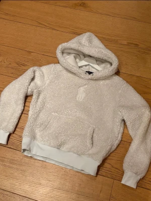 Polo Ralph Lauren teddy/fleece hoodie vit S - Mysig vit/beige teddy/fleece hoodie från Polo Ralph Lauren i storlek S. Bra skick, endast mindre tecken på användning. Snören saknas men kan enkelt ersättas. Passar perfekt till våren/sommaren.Hoodien har en stor huva, magficka och ribbade muddar vid ärmslut och nederkant. Perfekt för dig som vill ha en varm och stilren look med en soft vibe. Pris kan absolut diskuteras.