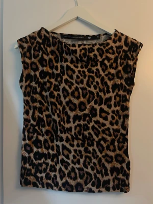 Leopardmönstrad ärmlös topp - Säljer en ärmlös topp från lager 157 med leopardmönster i bruna och svarta toner. Toppen har en rak och loose passform och är perfekt för dig som vill sticka ut med ett djärvt print. Materialet känns mjukt och lätt mot huden.