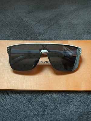 Lv glasögon  - Louis Vuitton Solglasögon – Monogram Lens  Exklusiva solglasögon från Louis Vuitton med ikoniskt monogrammönster ingraverat i glasen. Modern shield-design som ger en kraftfull och lyxig look.  Perfekt statement-accessoar för dig som vill sticka ut med stil och kvalitet i toppklass.  Skick: nytt skick!