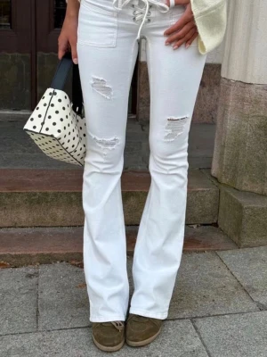 Vita bootcut jeans med slitningar - Snygga vita bootcut jeans med trendiga slitningar på låren och knäna. Hög midja med snörning framtill ger en cool detalj. Perfekta för dig som vill ha en fräsch och modern look. Använda runt 5ggr, skriv för egna bilder!!!💘💘