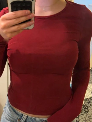 Mörkröd långärmad topp - Snygg mörkröd långärmad topp med rund halsringning och tight passform. Perfekt att matcha med jeans eller kjol för en stilren look. 