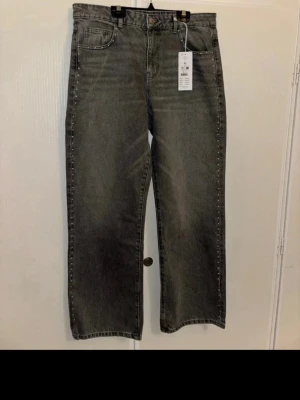 Grå raka jeans  - Gråa jeans mide waist / straight leg  Silvriga knappar på sidorna av byxorna   Säljer på grund av att de är för små för mig  Helt oanvänd köpta nyss   På bild 6 kan man se att de saknas två knappar längst ner på ena benet