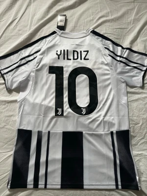 Juventus hemmatröja 25/26, Yildiz nr 10 - Juventus hemmatröja 25/26 från Adidas med Yildiz och nummer 10 på ryggen. Tröjan har serie A loggan på axeln och är i storlek M. 