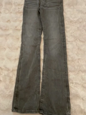 Grå bootcut jeans med slitning - Säljer ett par grå bootcut jeans med klassisk femficksdesign och lätt slitning. Jeansen har breda ben och normal midja, perfekt för dig som gillar en avslappnad och trendig look. Materialet är denim och färgen är tvättad grå. Storlek 170, pris 30kr