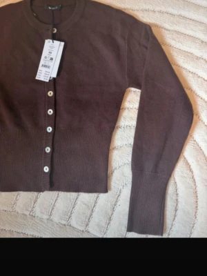 Brun ribbad kofta från Weekday - PRISLAPPEN ÄR INTE KVAR!! Brun kofta från Weekday med ribbade muddar och vita knappar framtill. Kort modell med långärmade ärmar och rund halsringning. Perfekt att matcha med jeans eller kjol för en snygg look.