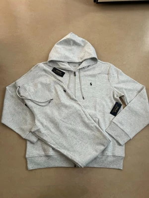 Ralph lauren tracksuit grå storlek large - Helt ny Ralph Lauren tracksuit (hoodie + byxor). En av de mest efterfrågade seten – perfekt för vardag och resor.  • Oanvänd / nyskick • Säljs som komplett set • Väldigt populär modell • Bekväm och stilren passform • Perfekt året runt  Storlek: L Färg: grå  Skickas snabbt 📦 Rabatt vid köp av flera plagg.