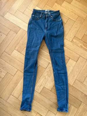 Blå skinny jeans med hög midja - Säljer ett par blå skinny jeans med hög midja och klassiska fem fickor. Jeansen har dragkedja och knapp framtill samt raka ben med smal passform. Från Lager 157 i modellen Snake.