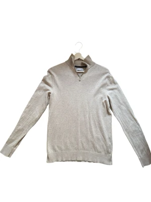 Beige polotröja i stickat material - Snygg beige stickad polotröja med lång ärm och ribbade muddar vid ärmslut och nederkant. Tröjan har en klassisk polokrage och är tillverkad i ett mjukt, tunt material som passar perfekt till lager på lager. Enkel och stilren design utan synliga loggor. Hör av er vid fler frågor eller funderingar. 