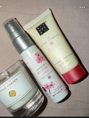 Rituals Sakura set med balm & spray - Ett mini set från Rituals med The Ritual of Sakura recovery hand balm i ljusgul tub med rosa kork, en Replenishing Laundry Spray i vit flaska med blommigt motiv och en doftljus från Savage Garden Collection i glasbehållare. Perfekt för dig som älskar fräscha och blommiga dofter.