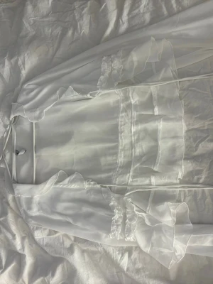 Vit transparent volangblus - Säljer en vit transparent blus med volangdetaljer och långa ärmar. Blusen har en romantisk känsla med tunna, skira material och fina rysch längs ärmar och bröst. Perfekt för dig som gillar en feminin och trendig stil.