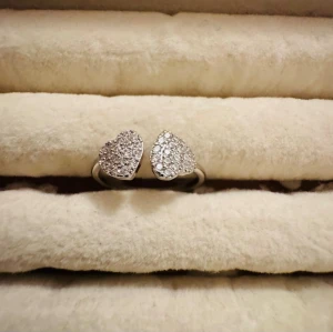 Silverring med två hjärtan - Säljer en snygg silverring med två hjärtformade detaljer som är täckta av gnistrande små stenar. Ringen har en öppen design och passar perfekt för dig som gillar stilrena accessoarer med lite extra bling.