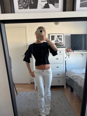 Svart croppad topp med volangärmar - Säljer en svart croppad topp med volangdetaljer på ärmarna. Toppen har en loose passning och är perfekt för dig som gillar en trendig och avslappnad stil. Materialet känns mjukt och lätt, och toppen har en enkel rund halsringning.