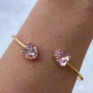 Bangle armband hjärtan kristall Light Rose - Armband, Bangle, i guldpläterad mässing med kristaller. Hjärtformade kristaller 11x10mm. Färg Light Rose ställbar storlek.  Jag skickar endast spårbart, samfraktar. Fast pris. Besök gärna mina övriga annonser.  Till mina smycken använder jag kristaller från Preciosa, Aurora och Swarowski.