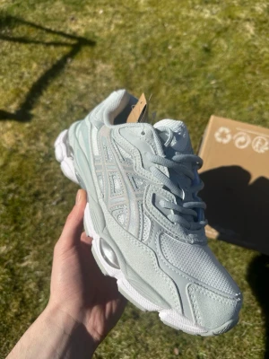 Ljusgrå Asics sneakers - Snygga ljusgrå sneakers från Asics med mesh och mocka detaljer. Skorna har klassisk Asics-logga på sidan och en chunky sula som ger en modern look. Perfekta för dig som gillar sportig stil och komfort.