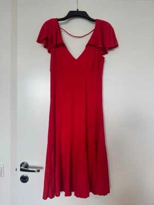 A|X Röd klänning med volangärmar strl M - Elegant klänning från Armani Exchange i en fin röd färg ❤️storlek M  - Klänningen har en smickrande passform med v-ringning och feminina volangärmar. Den figurnära överdelen och den lätt utsvängda kjolen gör att den sitter väldigt fint på kroppen – perfekt till fest eller sommarens tillfällen. Mjukt och bekvämt material. - Fint skick, men det finns en liten diskret fläck framtill vid bysten (se bild). Den är relativt svår att lägga märke till när klänningen bärs. 