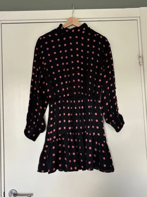 Prickig klänning  - Rosa prickig långärmad klänning. Har inbyggda shorts och uppknäppning med knappar på ena axeln och armen 