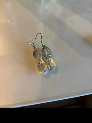 Infinite silver örhängen med pärldetaljer - Säljer ett par silvriga örhängen i form av infinite dekorerade med små pärlor längs framsidan. De har krokar för enkel användning och en elegant, glittrande look som sticker ut.