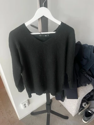 Svart stickad tröja från 157 - En svart stickad tröja från 157 i storlek XS. Tröjan har en enkel design med rund halsringning och långa ärmar. Materialet är mjukt och ger en avslappnad look, perfekt för att matcha med jeans eller kjol.