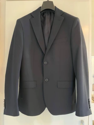 Mörkblå kostym i ”nyskick” säljes - Säljer sonens mörkblåa kostym av märket POUR. Han har bara använt dem vid ett tillfälle (vid skolavslutningen i 9:an i somras) så den är typ oanvänd. Fickorna på kavajen är tex inte uppsprättade. Min son var runt 165 - 170cm när han hade den. Skick som ny.