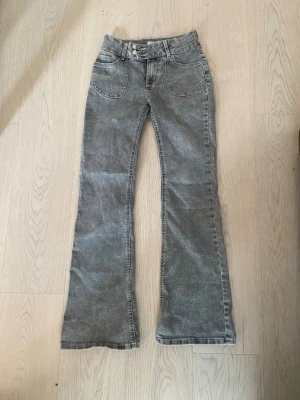 Grå bootcut jeans - Säljer ett par grå bootcut jeans i storlek 158/xxs med snygga broderade detaljer på bakfickorna. Jeansen har dubbla knappar i midjan och man kan anpassa dom hur man vill vid midjan, Såååå snygga 😍🙏🏼