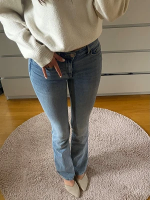 Ljusblå bootcut jeans - Säljer ett par ljusblå bootcut jeans med klassisk femficksdesign och normal midja. Jeansen har en snygg tvätt och är tillverkade i mjukt denimtyg med lite stretch för extra komfort. Perfekta för en avslappnad och trendig look.