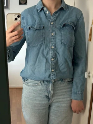 Jeansskjorta - Blå jeansskjorta från H&M i mycket fint skick. Två bröstfickor och knappar hela vägen upp. Material: Lyocell
