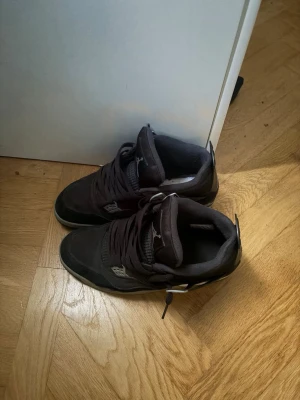 Svarta Air Jordan 4 sneakers - Säljer ett par svarta Air Jordan 4 sneakers med klassisk siluett och coola detaljer som meshpaneler och plastvingar. Skorna har vita inslag på sulan och Jumpman-loggan på tungan och hälen. Perfekta för dig som vill ha en ikonisk och sportig look.