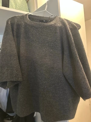 Grå stickad oversized tröja - En grå stickad tröja med oversized passform och rund halsringning. Tröjan har halvlånga ärmar och är tillverkad i ett mjukt och grovt stickat material. Perfekt för lager-på-lager och chill stil.
