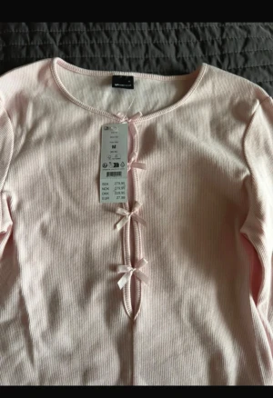 Ljusrosa ribbad topp med rosetter - Supersöt ljusrosa ribbad topp från Gina tricot  med långärmad design och tre små rosetter framtill. Toppen har en rund halsringning och är croppad, perfekt för att skapa en trendig look. 