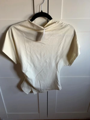 Ljusgul asymmetrisk topp från Gina Tricot  - Trendig ljusgul topp från Gina tricot med asymmetrisk design och korta ärmar. Tillverkad i mjuk bomull som känns skön mot huden. Perfekt för dig som gillar minimalistisk och modern stil.