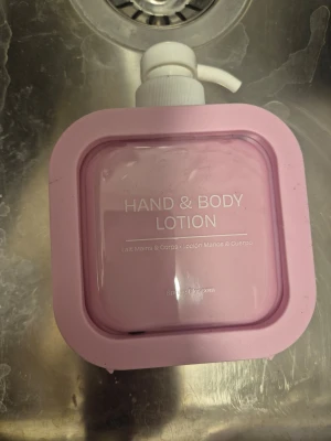 Hand & Body Lotion rosa pumpflaska - Hand & Body Lotion i en fyrkantig, ljusrosa plastflaska med vit pump. Texten på flaskan är vit och produkten har doften Spring Blossom. Perfekt för återfuktning av både händer och kropp. 300 ml