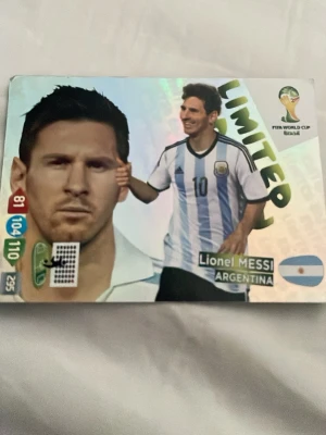 Panini Messi Limited Edition VM-kort - Samlarobjekt: Limited Edition fotbollskort från Panini Adrenalyn XL, FIFA World Cup Brasil. Kortet visar Lionel Messi i Argentinas landslagströja med blå och vita ränder. Kortet har färgglad design och officiell VM-logga.