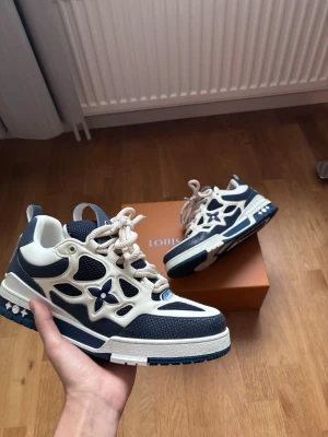 Louis Vuitton Skate - Snygga Louis Vuitton sneakers i blått och vitt med ikoniska LV-detaljer och blommönster på sidan. Skorna har snörning, meshpaneler och robust sula. Perfekta för dig som vill sticka ut med exklusiva och trendiga sneakers. 1:1KVALITET KOM DM FÖR FRÅGOR