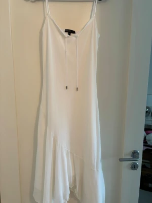 Vit Klämning med snörning - Säljer en vit klänning från KappAhl med tunna axelband och snörning framtill. Klänningen har asymmetrisk nederkant  som ger en flowy känsla. Perfekt för varma dagar och har en lätt, luftig passform.