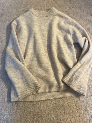 Beige stickad tröja - Mysig beige stickad tröja med rund hals och ribbade muddar vid ärmslut och nederkant. Tröjan har en avslappnad passform och är tillverkad i en mjuk ullblandning som passar perfekt för kyliga dagar.