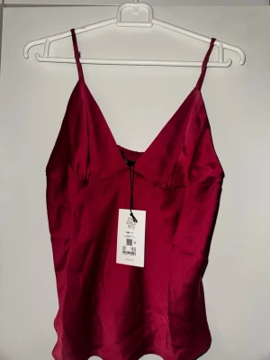Vinröd satin linnetopp från bikbok  - Snygg vinröd linnetopp från bikbok i glansigt satinmaterial. Toppen har smala justerbara axelband och v-ringning både fram och bak. Perfekt att styla med jeans eller kjol för en trendig look.