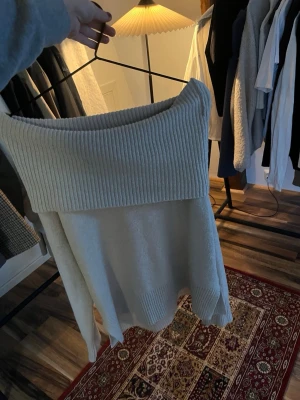 Off shoulder stickad tröja beige - Säljer en beige stickad tröja med bred off shoulder-krage i ribbstickat material. Tröjan har lång ärm och en lös, avslappnad passform som ger en chill vibe. Perfekt för lager på lager under kalla dagar.