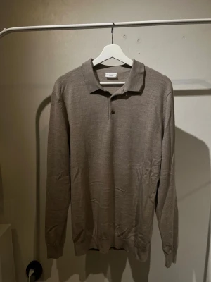 Brun långärmad pikétröja John Henric - Snygg brun långärmad pikétröja från John Henric. Tröjan har klassisk krage, två knappar framtill och är tillverkad i ett tunt, mjukt material som ger en clean look. Perfekt för dig som gillar stilrena och tidlösa plagg.