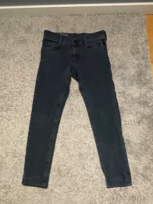 Svarta slim fit jeans från Nudie - Säljer ett par svarta slim fit jeans från Nudie Jeans med klassisk femficksmodell och diskret broderad bakficka. Jeansen har normal midja och är tillverkade i stretchigt denim för skön passform. Perfekta till en avslappnad stil.