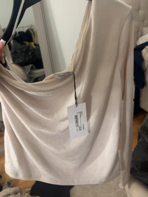 Beige långärmad topp från Stockh lm - Trendig beige långärmad topp från Stockh lm med snygg drapering framtill. Toppen har en croppad passform och är tillverkad i ett mjukt, stretchigt material som känns skönt mot huden. Perfekt att styla med höga jeans eller kjol.