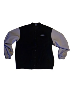 No Fear svart och grå bomberjacka - Säljer en klassisk collegejacka från No Fear med svart kropp och beigea armar. Jackan har tryckknappar framtill och en liten No Fear-logga på bröstet. Perfekt för dig som gillar streetwear och retrostil.