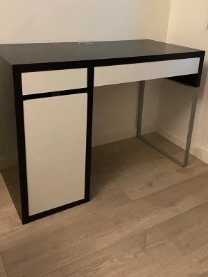 IKEA Micke skrivbord svartbrun/vit - Snyggt och stilrent skrivbord från IKEA, modell Micke, i svartbrunt och vitt. Bordet har en låda och ett skåp på vänster sida samt en praktisk kabelgenomföring på bordsskivan. Perfekt för plugget eller hemmakontoret.
