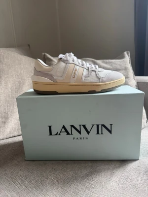 Snygga helt nya Lanvin sneakers - Snygga vit, grå beiga sneakers från Lanvin med beige sula och klassisk retrodesign. Skorna har detaljer i läder och textil, samt Lanvin-logga på sidan. Perfekta för dig som gillar stilrena och exklusiva sneakers med en modern touch.
